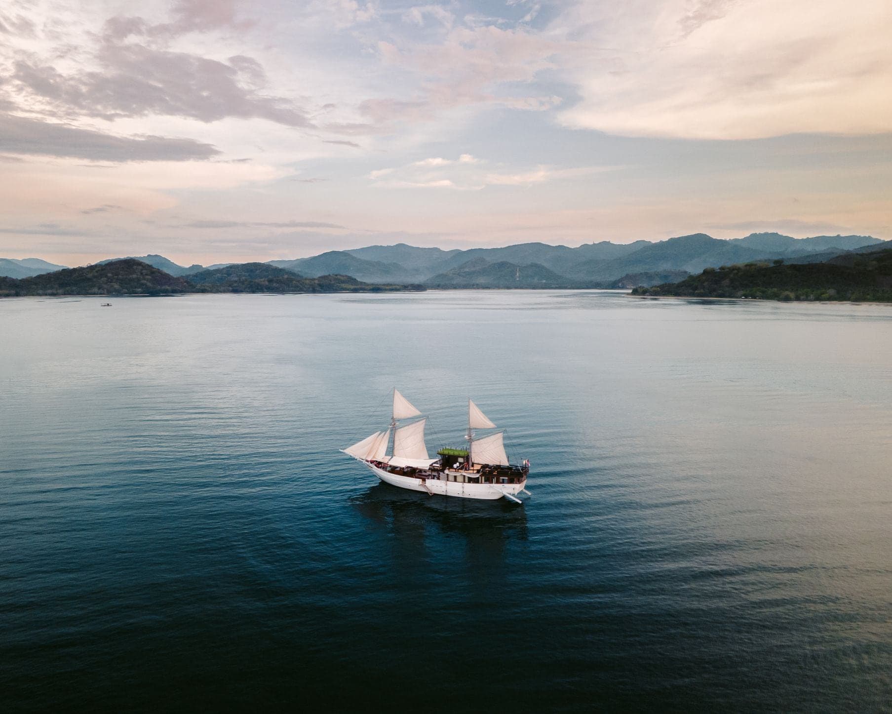 A traditional phinisi with sails up at golden hour in Komodo National Park